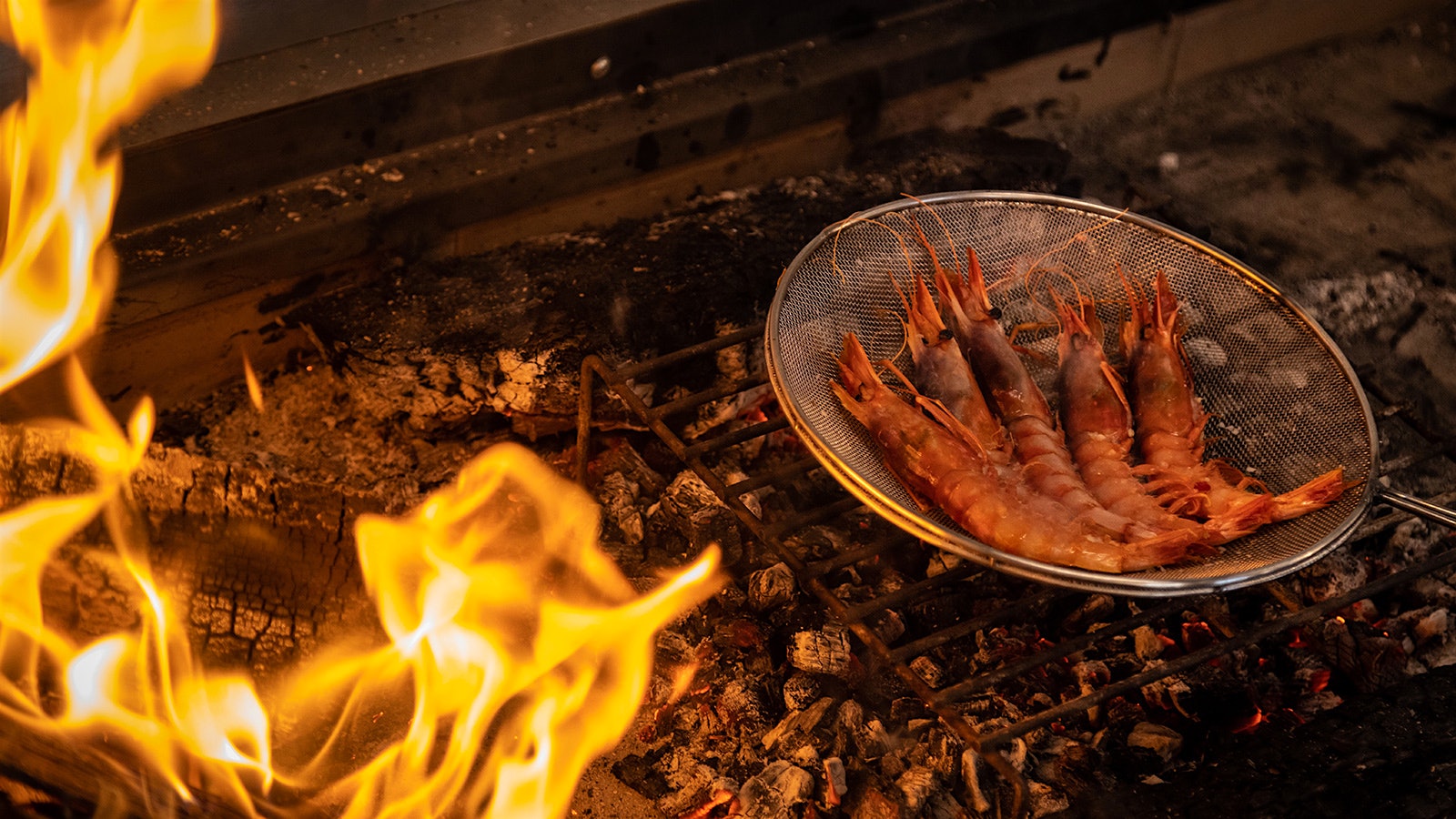 Prawns in a pan over a hot grill with an open flame
